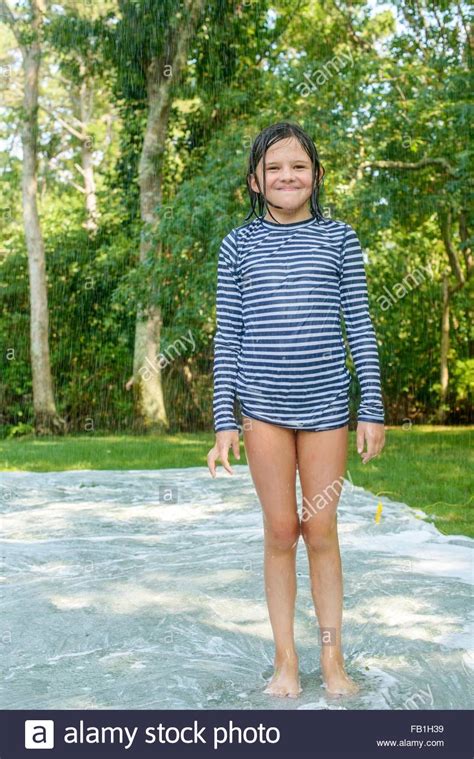 Portrait of young girl standing on slip n slide water mat ...